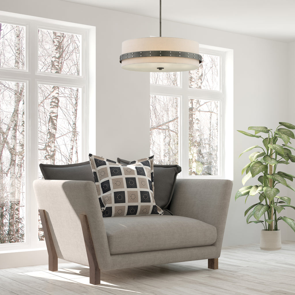 Gray armchair with patterned and solid cushions in a room with large windows and a plant.