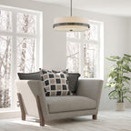 Gray armchair with patterned and solid cushions in a room with large windows and a plant.